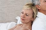 Middle-aged couple sitting back to back in bedroom, close-up