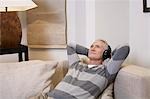 Middle-aged man listentening to music on headphones in living room