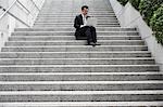 China, Hong Kong, business man sitting on steps using laptop, low angle view