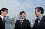 Three business men smiling, office buildings in background