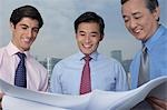 Three business men holding and looking at blueprints, smiling