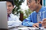 Two business man using laptop sitting in outdoor cafe, close up