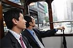 China, Hong Kong, two business men sitting in double Decker tram, side view