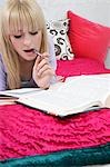 Teenage girl (16-17) se trouvant sur le lit, fait ses devoirs