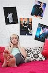 Teenage girl (16-17) sitting on bed, listening to music, eyes closed