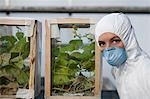 Worker in protective mask and suit by plants, portrait