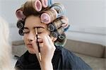 Model in Hair Curlers Having Makeup Applied