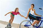 Young woman on bike pulling young woman on rollerblades