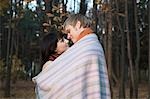 Young couple wrapped in blanket, embracing in forest