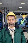 Serious man standing in factory, wearing hart hat