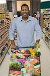 Mature man stands with grocery shopping in supermarket aisle