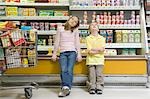 Brother and sister sit side by side on fridge counter in supermarket