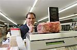 Mature man looks at selected meat on weighing machine