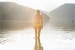 Woman in yellow bikini stands at edge of lake