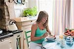 Pregnant woman sitting at kitchen table eating breakfast