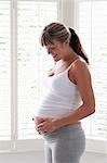 Pregnant woman standing near window touching stomach