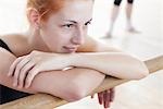 Young woman leans on ballet barre at mirror in rehearsal room