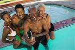 Senior couple and mid-adult couple posing for mobile phone photograph at swimming pool, elevated view.