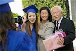 Graduate videotaping other graduate with mother and grandfather outside