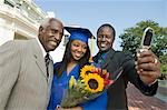 Graduate with father and grandfather taking picture with cell phone outside university