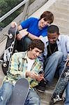 Three skateboarders sitting on stairs using cell phone