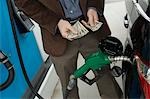 Man counting money over gas pump in car, mid section