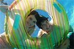 Boy and girl looking through inflatable raft in swimming pool, underwater view