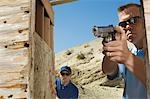 Man watching colleague aiming hand gun at firing range