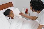 Nurse taking temperature of girl (7-9) lying in bed