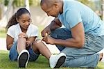 Father applying bandaid to daughter (7-9) in park