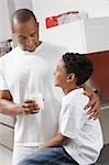 Father holding glass of milk, embracing son (7-9) indoors