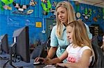 Schulmädchen mit Computer mit Lehrer im Klassenzimmer