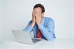 Studio shot of businessman with head in hands using laptop