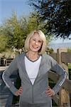 Mature adult woman stands smiling, in tracksuit with hands on hips