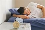 Man Sleeping in Bed with Alarm Clock on Bedside Table