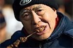 China,Beijing. Chinese New Year Spring Festival - Changdian street fair - an elderly man eating shish kebab.