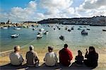 Eine Gruppe Touristen plaudern und essen Eis beim Sitzen auf dem Kai in St Ives, Cornwall.