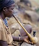 An old Konso woman with facial scarification smokes a traditional pipe made in part from a small decorated gourd. Tobacco is grown locally by the Konso.