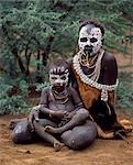 A Karo woman sits with child. A small Omotic tribe related to the Hamar,who live along the banks of the Omo River in southwestern Ethiopia,the Karo are renowned for their elaborate body painting using white chalk,crushed rock and other natural pigments. Typically for a Karo woman,the mother has ochred her hair in tight ringlets and has a ring through her bottom lip.