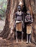 Deux jeunes filles de Karo se tenir devant le tronc massif d'un figuier. Une petite tribu Omotic associés à Hamar, qui vivent le long des rives du fleuve Omo en Éthiopie le sud-ouest, le Karo sont renommés pour leur peinture sur corps élaborés à l'aide de craie blanche, la pierre concassée et autres pigments naturels.