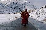 Tibet,Kham,Pomda. A monk strolls down the road near his local monastery. Sudden storms can block roads well into spring and early summer.