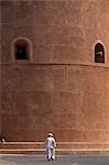 An old Omani man walks beneath the imposing watchtower of Al Hazm Castle. The magnificent 18th century military stronghold makes full use of traditonal Omani defensive features boasting a massive wooden entry door,secret escape tunnels,dungeons,cannon towers,gun ports and a machicolation for pouring boiling date syrup on attackers.