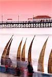 Totora (Reed) Boote werden entlang des Strandes, mit die hölzerne Pier im Hintergrund Dorf Angeln in Huanchaco, nahe Trujillo im Norden Perus gestapelt.