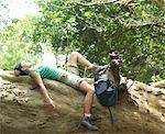 Young woman resting on rock formation in forest, side view