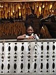 Une fille malgache avec épis de maïs suspendus pour sécher du balcon d'une maison de deux étages typique de Betsileo, Madagascar.