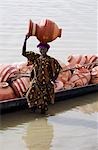 Mali,Djenne. A woman potter unloads her pots from a traditional wooden pirogue to sell at Djenne market. The weekly Monday market is thronged by thousands of people and is one of the most colourful in West Africa.