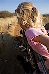 Région de Erongo Damaraland, Namibie. Une jeune fille, ses cheveux soufflant dans le vent, se penche sur le côté d'un véhicule de safari comme il pousse dans des pâturages sur une piste de jeu