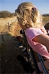 Namibia,Damaraland,Erongo Region. A young girl,her hair blowing in the wind,leans over the side of a safari vechicle as it drives through grassland on a game track