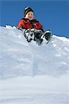 Norway,Tromso,Lyngen Alps. Young boy sits on a tobogganing seat to slide down a steep snow bank in bright winter sunshine