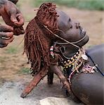 A Samburu warrior has his Ochred hair braided by a friend. A mixture of cow's urine and ashes is often rubbed into the hair first to help straighten it. The wooden headrest is used as a pillow at night. Long braids of Ochred hair distinguish warriors from other members of their society. The warriors are vain and proud,taking great trouble over their appearance.